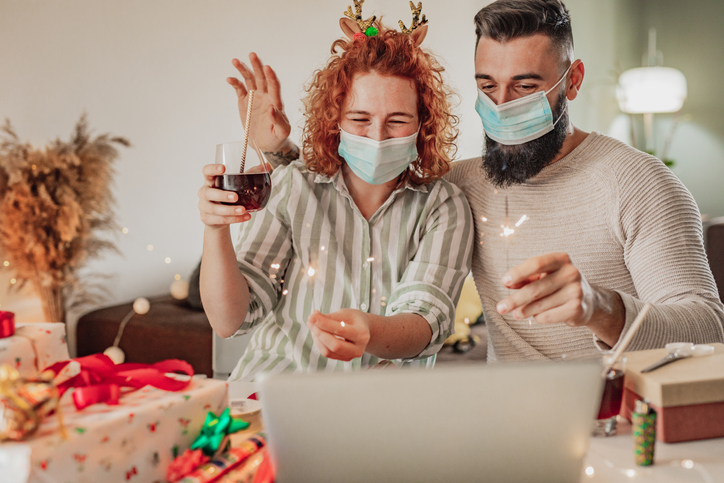 Happy couple with face masks celebrating winter holidays online on a video cal