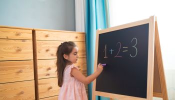 Little girl is studying math on the blackboard in her room