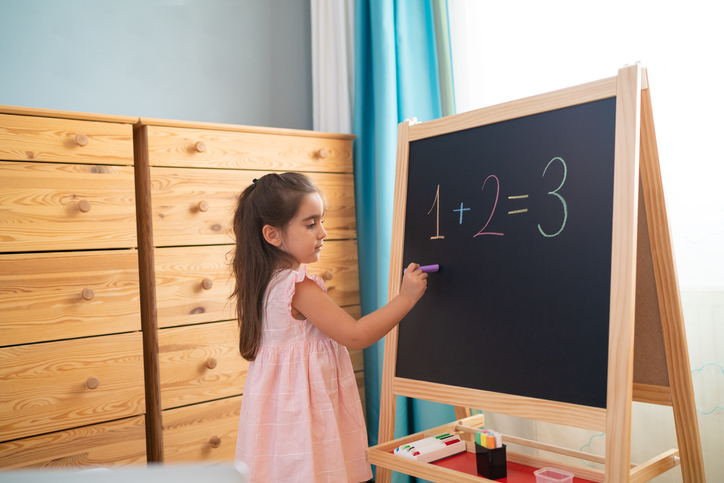 Little girl is studying math on the blackboard in her room