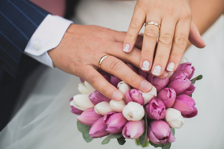 Hands of the bride and groom on a beautiful wedding bouquet with pink and white flowers, green leaves. Newlyweds on their wedding day.
