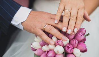 Hands of the bride and groom on a beautiful wedding bouquet with pink and white flowers, green leaves. Newlyweds on their wedding day.