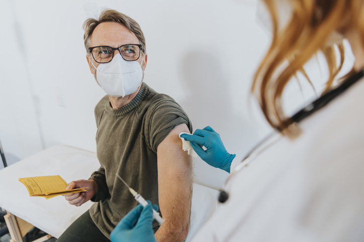 Healthcare worker with COVID-19 vaccine dose preparing patient arm for vaccination at examination room