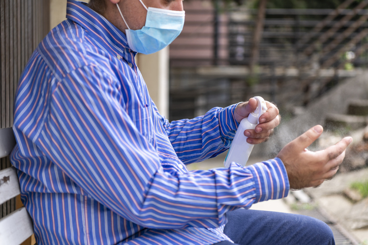 Businessman with Surgical Face Mask is Sitting in the Backyard and Cleaning his Hands.