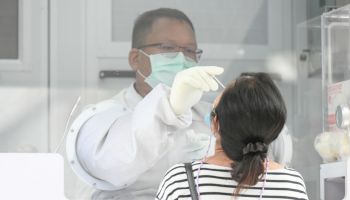 A health worker collects a nasal swab sample from a woman...