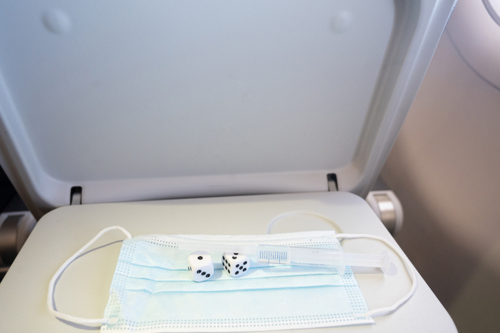 Travel in times of pandemic. Syringe with vaccine on two dices on a surgical mask on a passenger's seat tray inside an airplane.