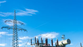 An electrical transformer and a high-voltage mast against a blue sky.