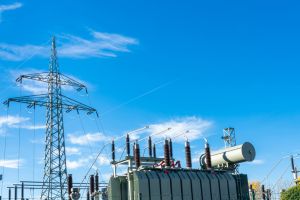 An electrical transformer and a high-voltage mast against a blue sky.