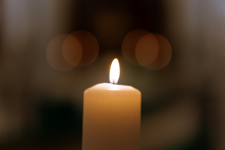 Single burning candle with soft bokeh lights peaceful warm flame symbolizing prayer, remembrance, faith and hope in dark background