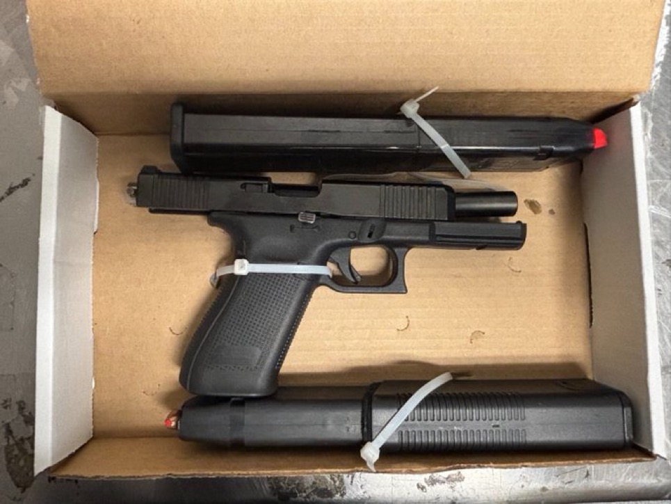 A black handgun and two magazines in a cardboard box.