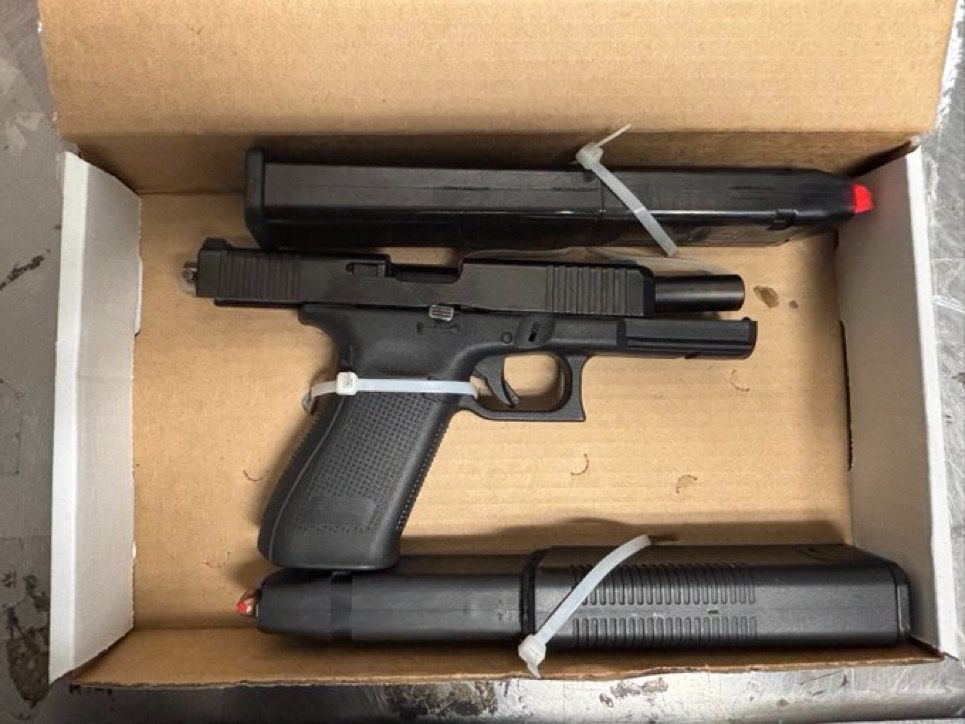 A black handgun and two magazines in a cardboard box.