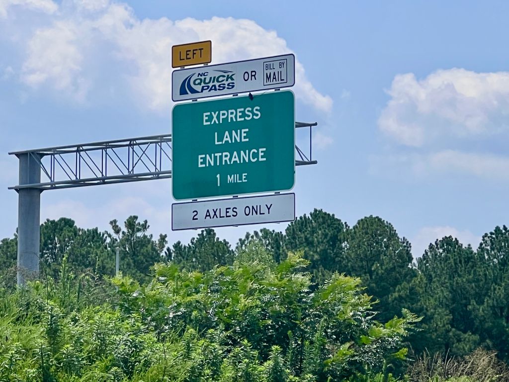Green highway sign indicating "EXPRESS LANE ENTRANCE 1 MILE" with "2 AXLES ONLY" and "NC QUICK PASS OR BILL BY MAIL" text.