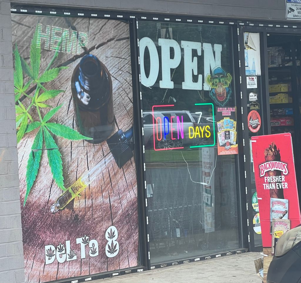 A storefront window displays a "OPEN" sign and "OPEN DAYS" text, with cannabis-related imagery and branding.