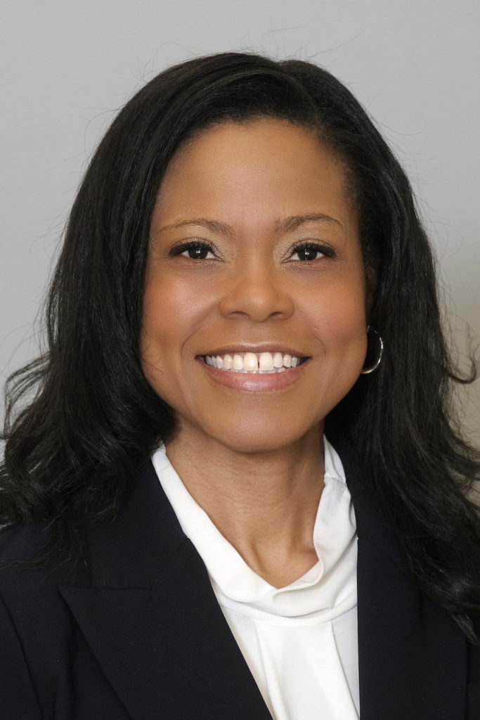 Headshot of a smiling middle-aged woman with long dark hair wearing a black blazer and white blouse.